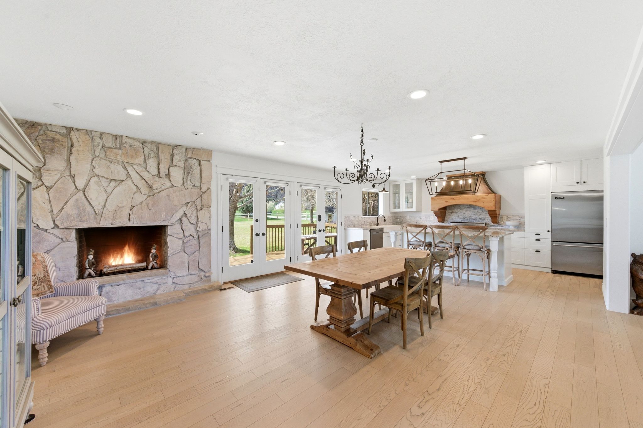 Dining area with a stone fireplace lit, open to kitchen and yard doors
